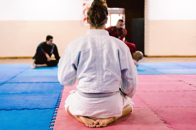 Young Latino and Hispanic male with long hair sitting on his legs on a tatami floor watching a jiujitsu fight