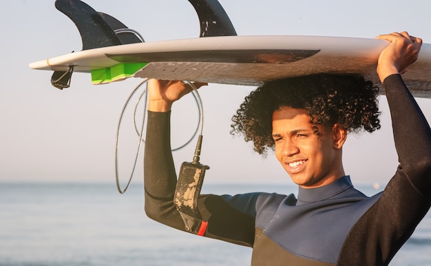 Young Latino surfers carrying surfboard on head with sea in background. A cheerful young afro. Extreme water sport concept. Summer vacation idea. Sunny day