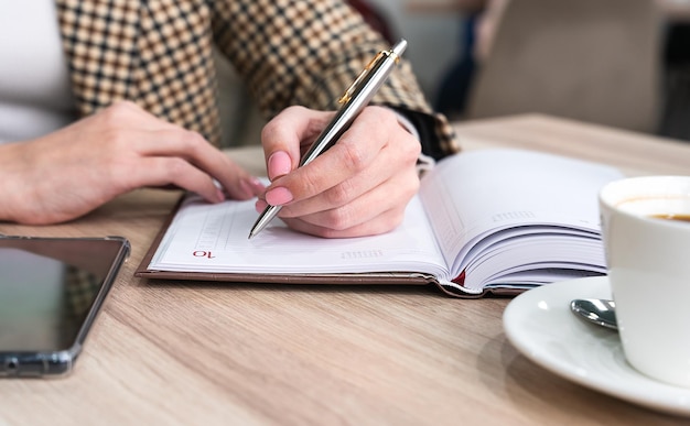 A young lefthanded girl writes a plan for the day in a notebook while sitting in a cafe Closeup