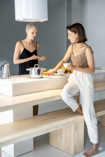 Young lesbian couple cooking healthy vegetarian food at modern kitchen. Healthy eating, homosexual relations and lifestyle at home concept