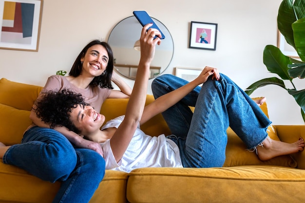 Young lesbian couple taking selfie at home living room using mobile phone