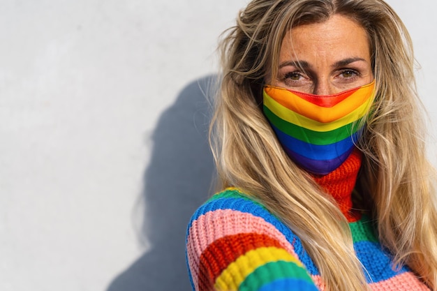 Young lesbian smiling on camera while wearing rainbow face mask to protect others for Coronavirus pandemic Focus on face