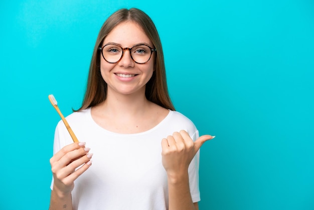 Young Lithuanian woman brushing teeth over isolated background pointing to the side to present a product