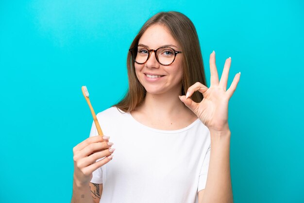 Young Lithuanian woman brushing teeth over isolated background showing ok sign with fingers