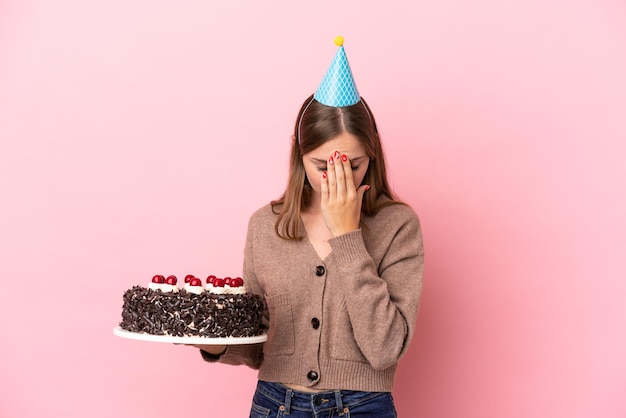 Young Lithuanian woman holding birthday cake isolated on pink background with tired and sick expression