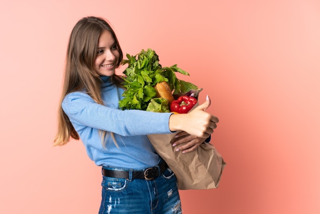 Young Lithuanian woman holding a grocery shopping bag giving a thumbs up gesture