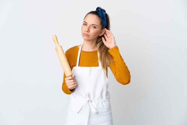 Young Lithuanian woman holding a rolling pin isolated on white wall having doubts