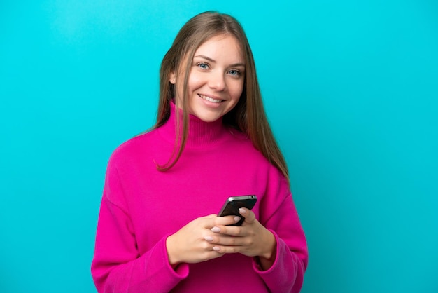 Young Lithuanian woman isolated on blue background sending a message with the mobile