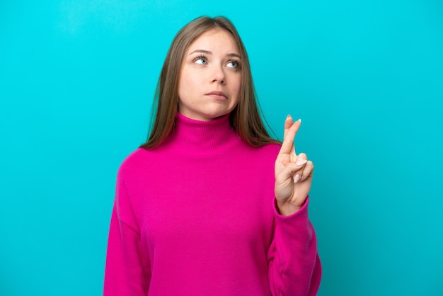 Young Lithuanian woman isolated on blue background with fingers crossing and wishing the best