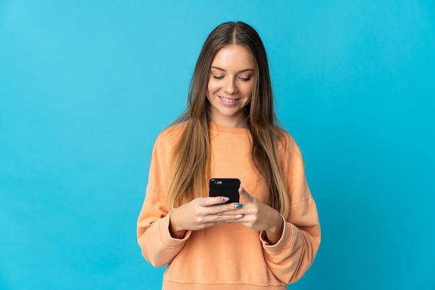 Young Lithuanian woman isolated on blue wall sending a message or email with the mobile