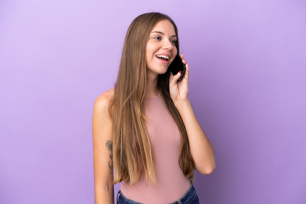 Young Lithuanian woman isolated on purple background keeping a conversation with the mobile phone