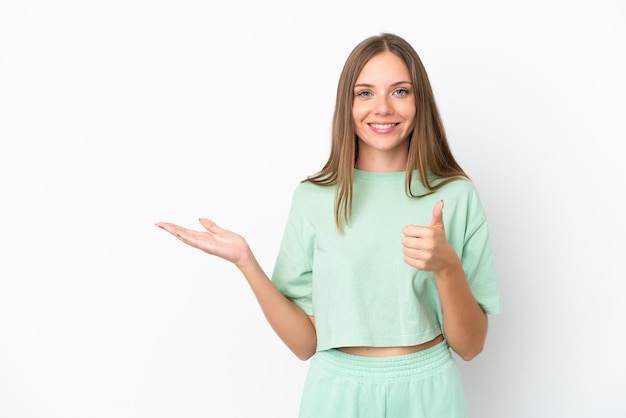 Young Lithuanian woman isolated on white background holding copyspace imaginary on the palm to insert an ad and with thumbs up