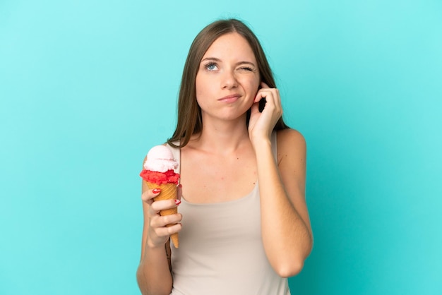 Young Lithuanian woman with cornet ice cream isolated on blue background frustrated and covering ears