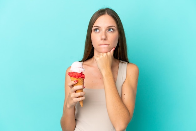 Young Lithuanian woman with cornet ice cream isolated on blue background having doubts and thinking