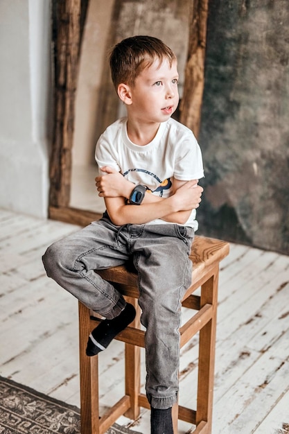 Young little caucasian child with green eyes wearing a white tshirt holding a wristwatch looking away with a relaxed expression