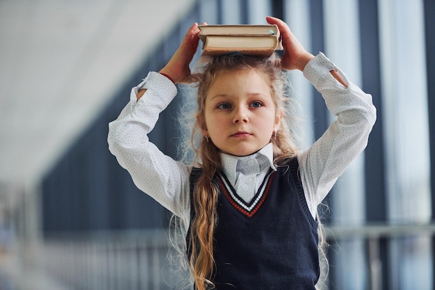 Young little school girl in uniform standing in hallway with books