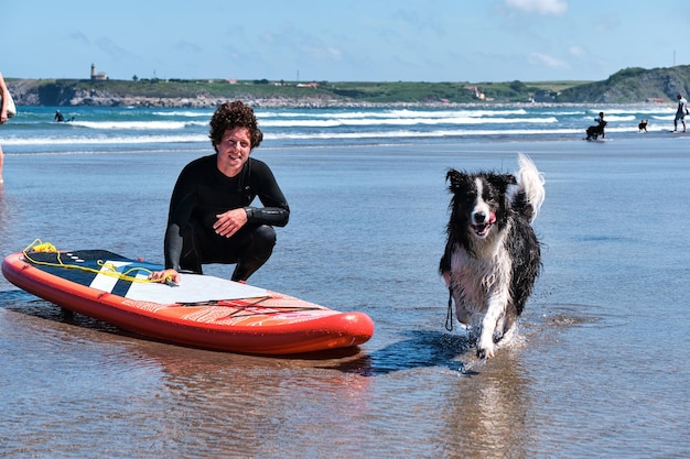 Young long curly hair surfer posing with his border collie dog while it is running