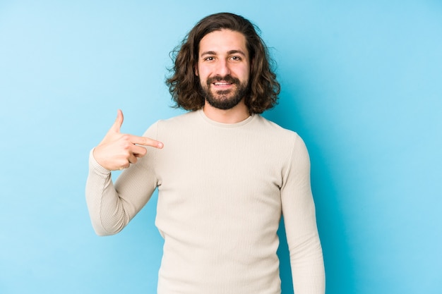 Young long hair man isolated on a blue person pointing by hand to a shirt copy space, proud and confident