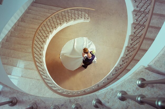 young lovely married couple stand under the ladder in wedding suits