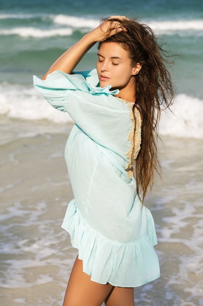 Young lovely woman wearing beautiful blue dress  is walking by the sea shore