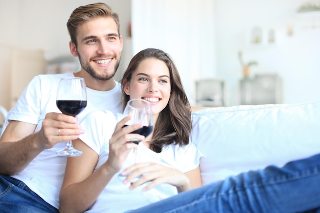 Young loving couple drinking a glass of red wine in their living room.