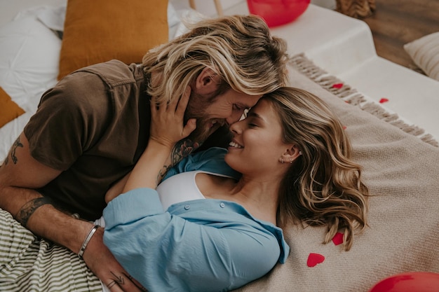 Young loving couple embracing and kissing while lying in bed surrounded with heart shape balloons