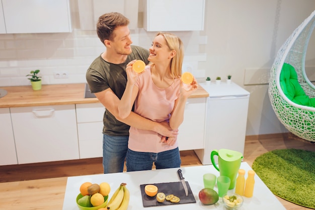 Young loving couple has fun with organic orange while cooking together fresh fruits in white kitchen. Healthy food. Happy family. Healthy eating