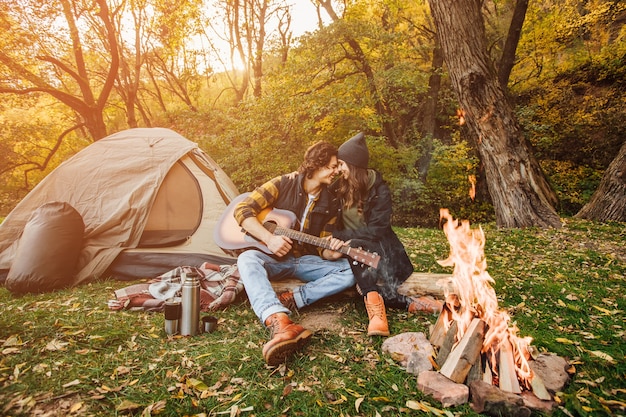 Young loving couple of tourists relaxing near the bonfire in the nature