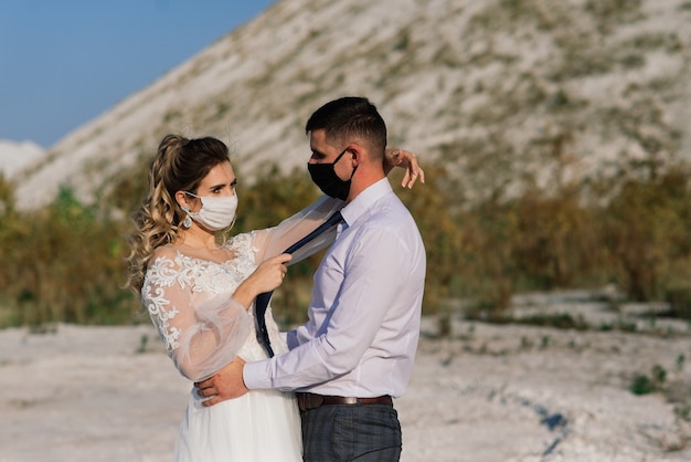 Young loving couple walking in medical masks in the park during their wedding day.