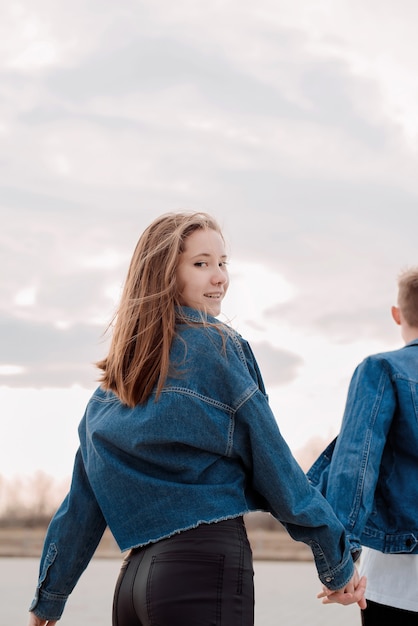 Young loving couple wearing jeans spending time together in the park having fun, woman holding hands with her boyfriend looking back