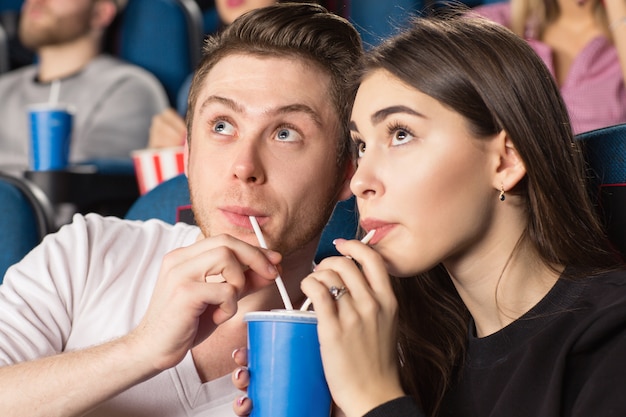 young loving drinking the same drink together with two straws in watching movies at the local cinema