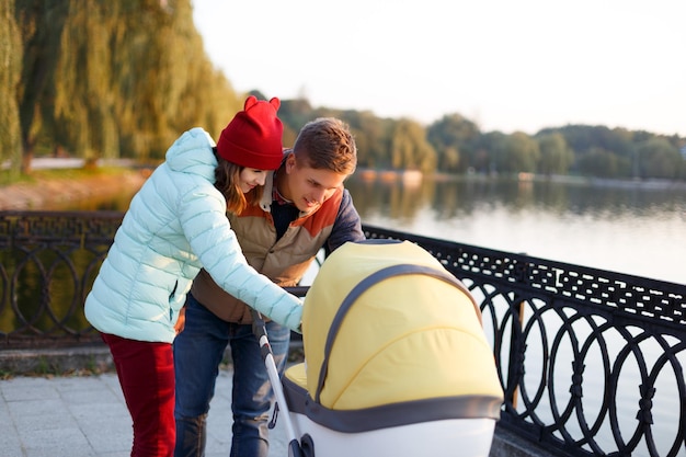 A young loving family walks by the lake with a stroller smiling parents couple with baby pram in