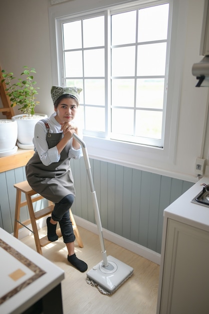 A young maid cleaning the house with a mop There is a kitchen backdrop