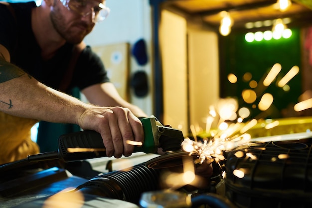 Young maintenance service worker with electric handtool grinding details of engine