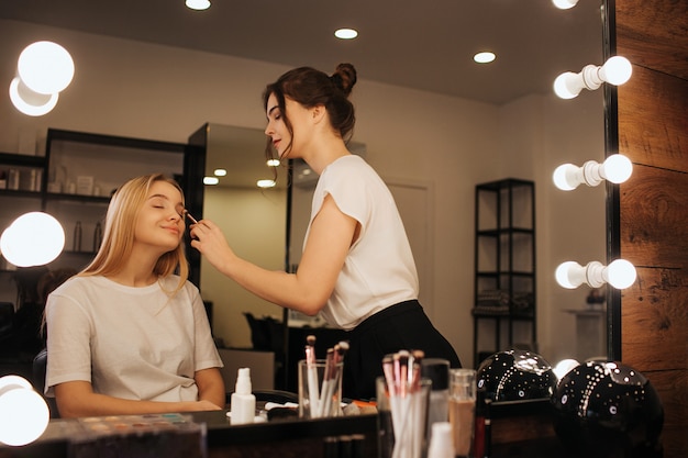 Young makeup artist put makeup of young woman's face