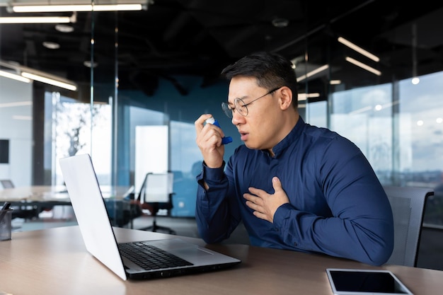 Young male asian office worker having asthma attack at workplace breathing hard he sits at a table