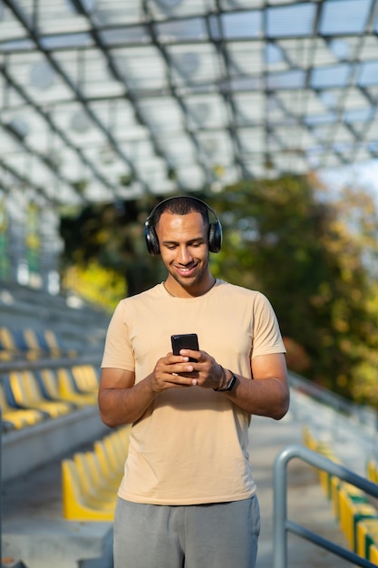 A young male athlete is standing at the stadium wearing headphones and holding a phone will do