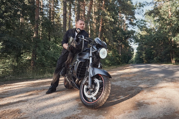 Young male biker travels on a motorcycle alone stopped on the side of a forest road