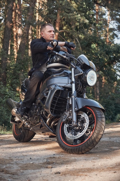 Young male biker travels on a motorcycle alone stopped on the side of a forest road