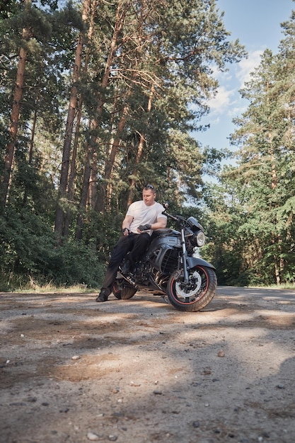 Young male biker travels on a motorcycle alone stopped and smoking on the side of a forest road