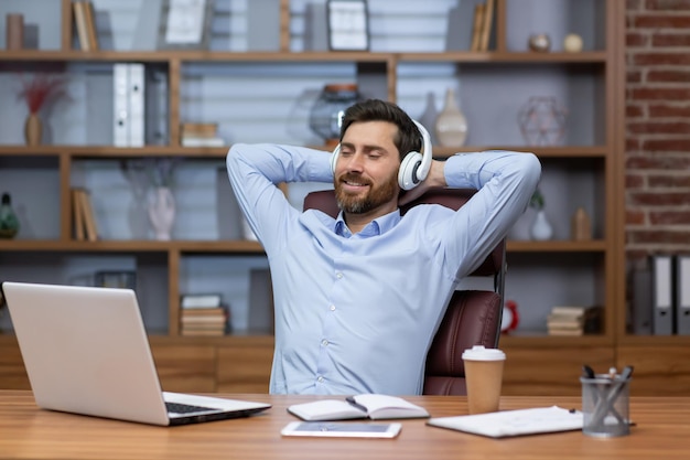 A young male businessman is sitting in the office in a chair at the desk he put his hands behind his