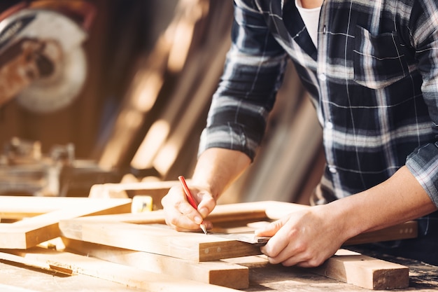 A young male carpenter builder working overall equals a wooden bar with a milling machine in the workshop, 