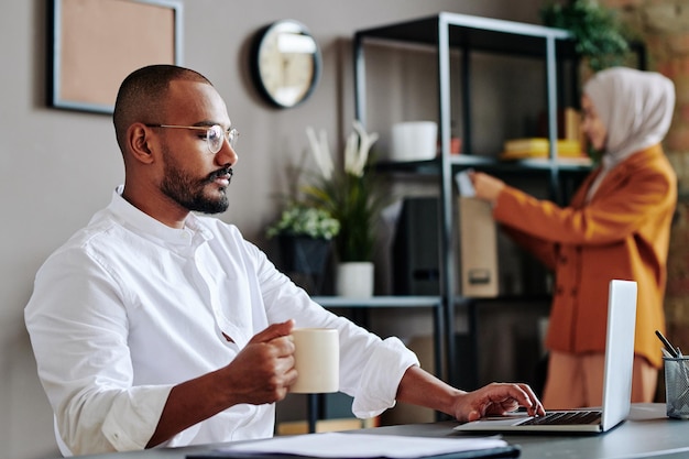 Young male ceo in white shirt looking at laptop screen against female colleague