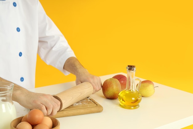 Young male chef cooking on yellow background