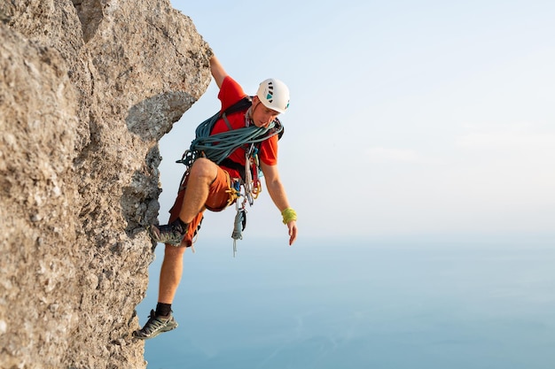 Young male climber climbs a difficult route with a view of the sea at sunset