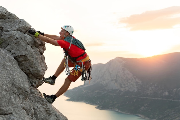 Young male climber climbs a difficult route with a view of the sea at sunset