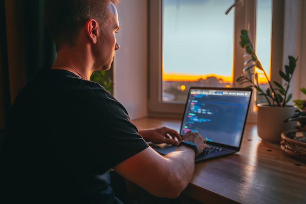 A young male developer is programming a code script late at night with beautiful city lights