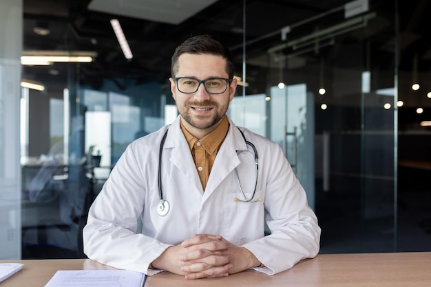 A young male doctor conducts a video conference online consultation records a medical podcast runs a medical blog Sitting in an office in a hospital and smiling at the camera