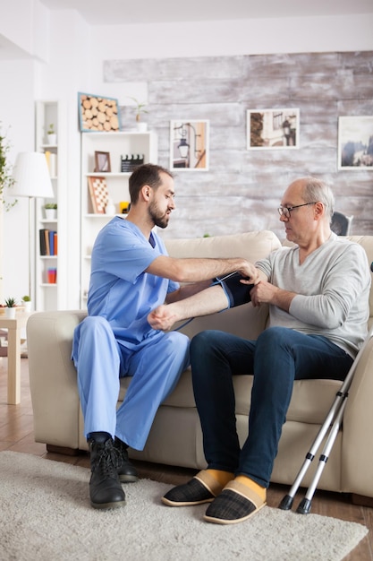 Young male doctor in nursing home taking blood pressure of elderly age male.