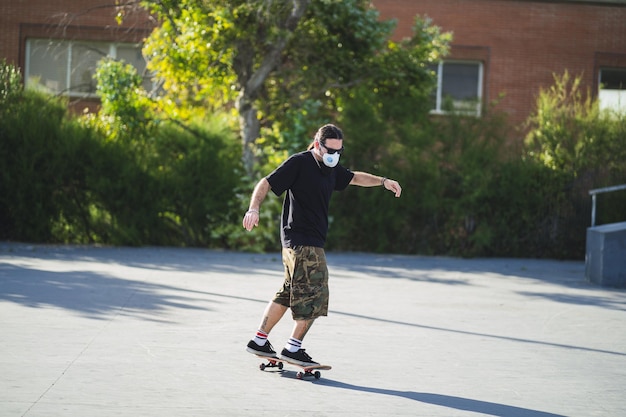 Young male doing different tricks with a skateboard in the park wearing a medical face mask